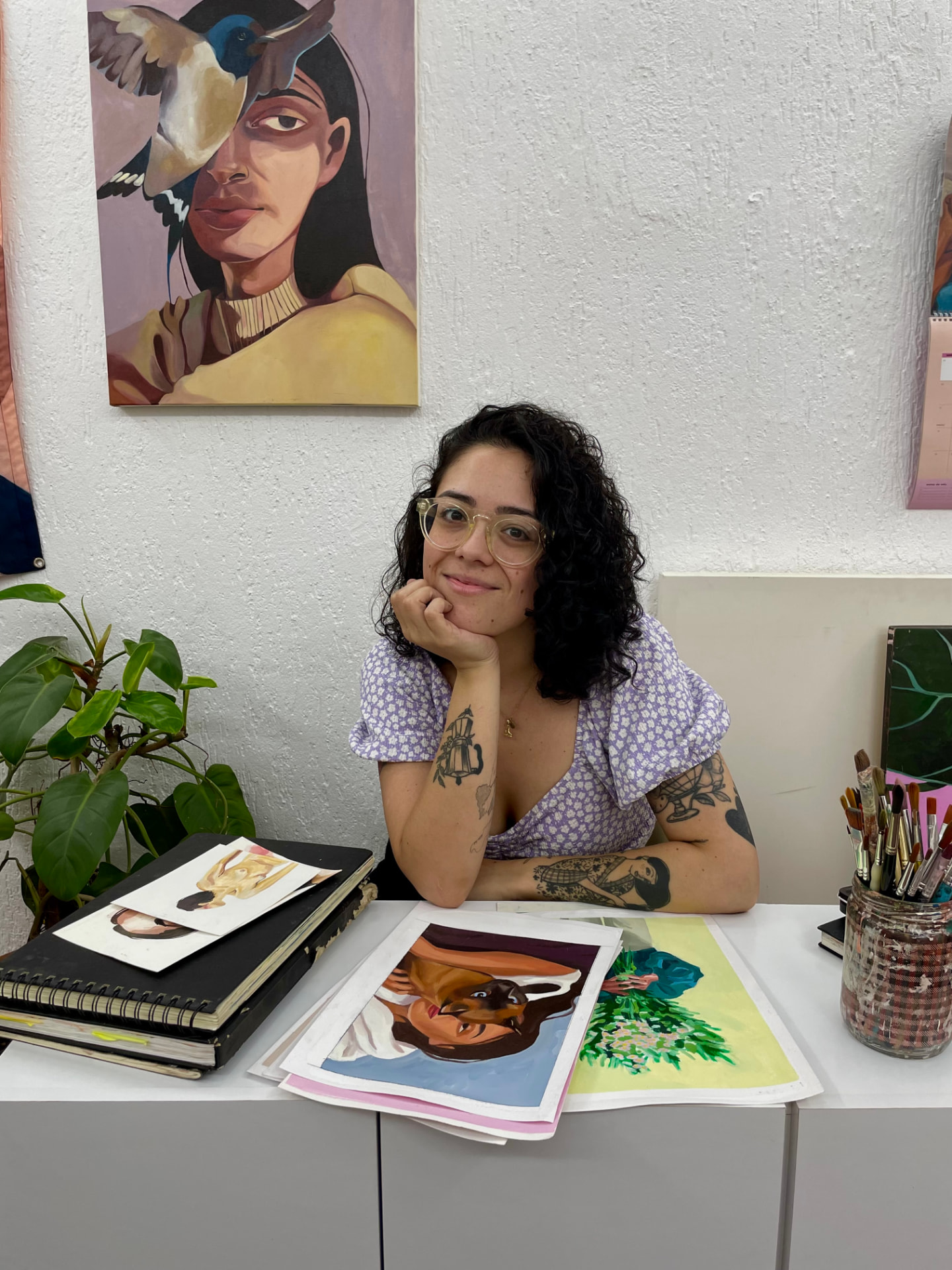 Brunna Mancuso no estúdio, com pinturas e materiais de trabalho ao redor